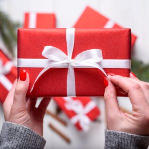 Close up of young woman hands holding red Christmas present above white wooden background. Christmas background with red gift boxes. Flat lay, top view
